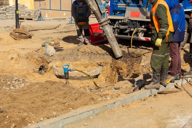 Workers use a suction excavator based on a truck to sample soil in a well for communications