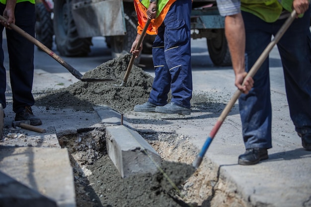 Workers with uniforms filling the hole with cement for installing a sidewalk