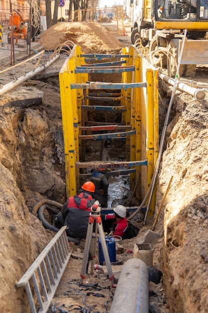 Workers working at deepening supported by trench box with pipe bedding pea gravel during installation of drainage pipe