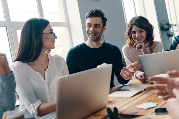 Working as a team. Group of young modern people in smart casual wear discussing something and smiling while working in the creative office