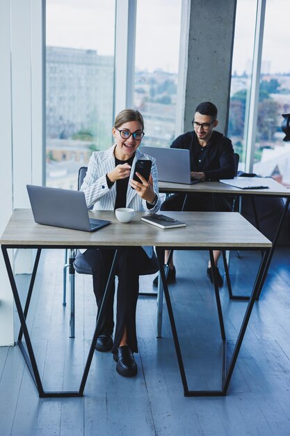 Working atmosphere in an office with large windows A female manager is sitting at a desk using a laptop in a modern office against the background of a colleague