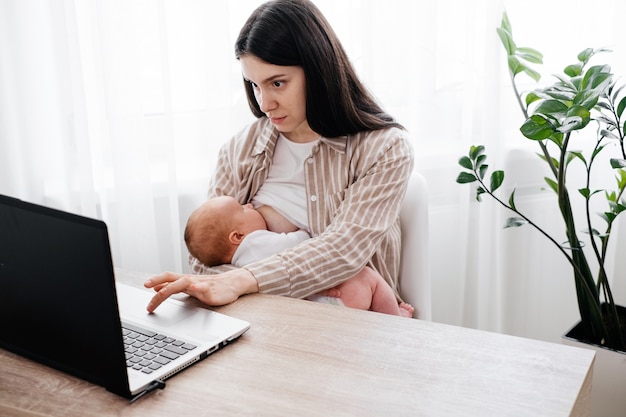 Working breastfeeding woman with infant near laptop