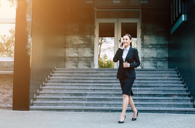 Working business conversation A modern smiling business woman in a black suit is walking down the street and talking on the phone with a client