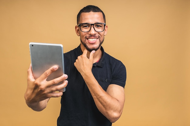 Working on digital tablet Portrait of happy smiling young African american black man holding digital tablet while standing isolated over beige background