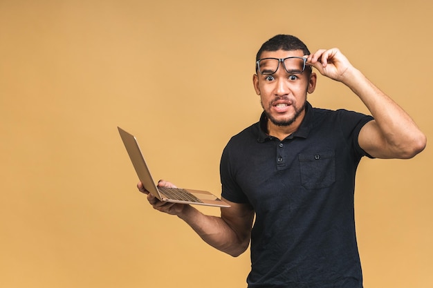 Working on digital tablet Portrait of shocked amazed surprised young African american black man holding digital tablet while standing isolated over beige background