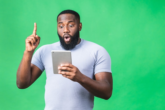 Working on digital tablet. Portrait of young African american black man holding digital tablet while standing isolated over green background.