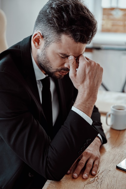 Working late. Tired young man in formalwear massaging nose while sitting in the office