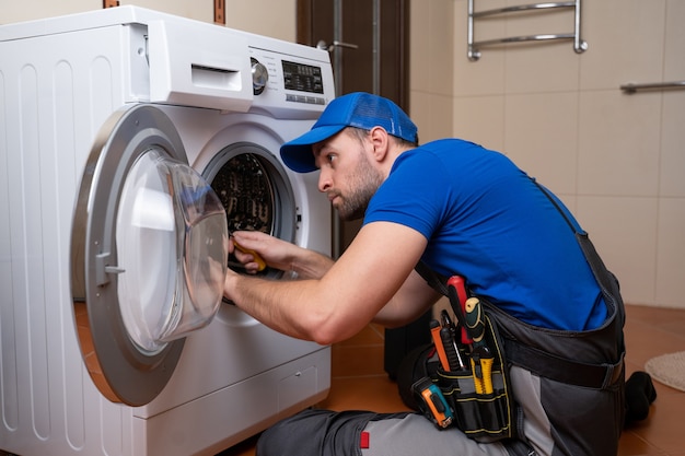 Working man plumber repairs a washing machine in home washing machine installation or repair plumber connecting appliance