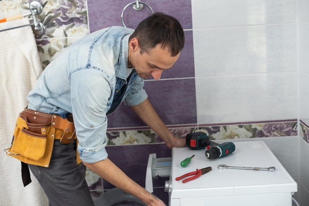 working man plumber repairs a washing machine in laundry.