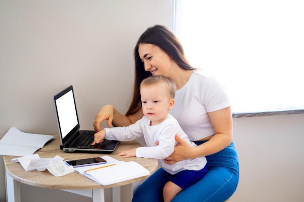 Working mother concept Young woman working on laptop with her child from home