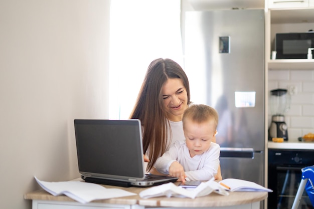 Working mother concept Young woman working on laptop with her child from home