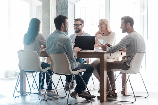 Working on new project together. Group of confident business people in smart casual wear working together while sitting at the desk in office