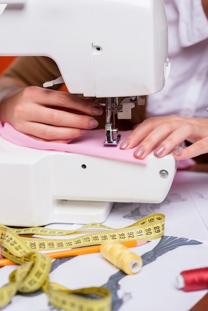 Working on sewing machine. Close-up of female fashion designer working on sewing machine while sitting at her working place