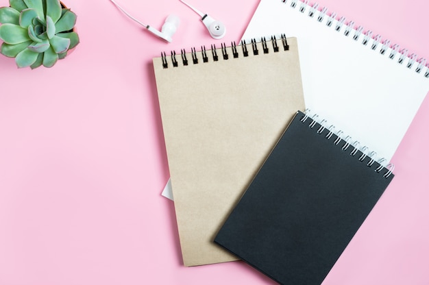 Working space: notepads, headphones and succulent flower on pink background. 