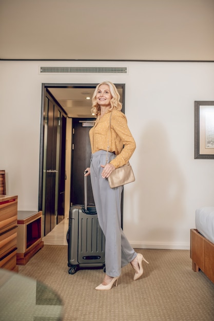 On a working trip. Elegant blonde woman in grey pants standing in a hotel room