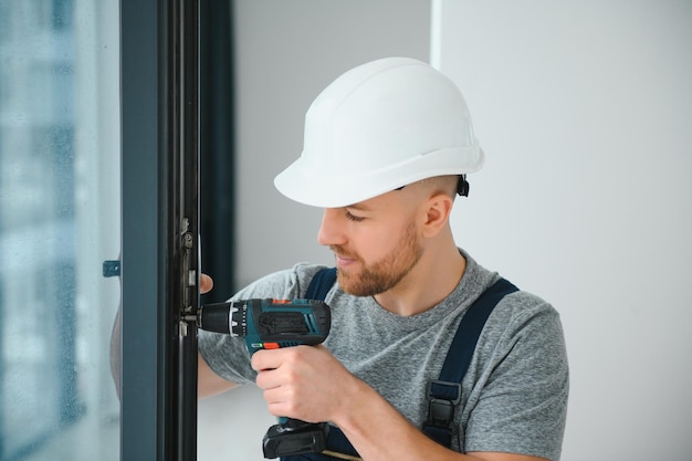 Workman in overalls installing or adjusting plastic windows in the living room at home