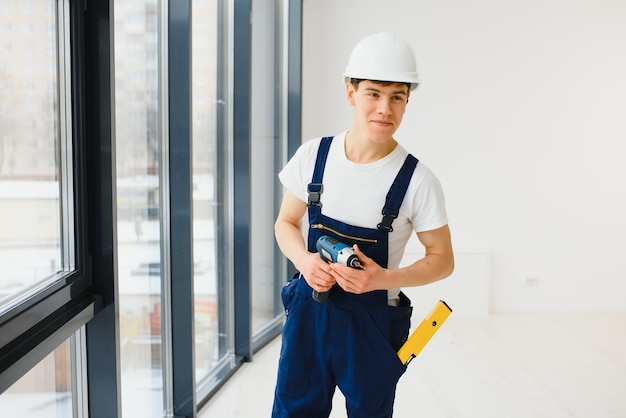 Workman in overalls installing or adjusting plastic windows in the living room at home