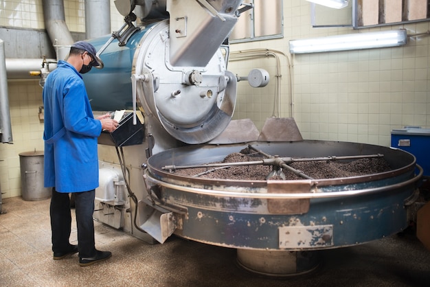 Workman standing at roasting machine. View of coffee roaster working on roasting equipment.