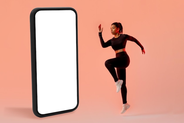 Workout application concept Slim lady exercising near big cellphone jumping in studio over neon background mockup