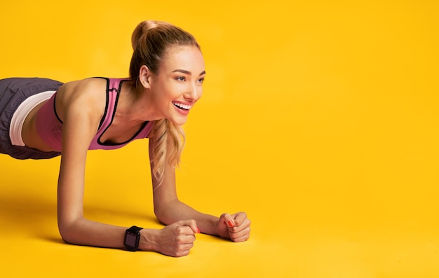 Photo workout fitness girl doing plank exercise and smiling over pink studio background free space