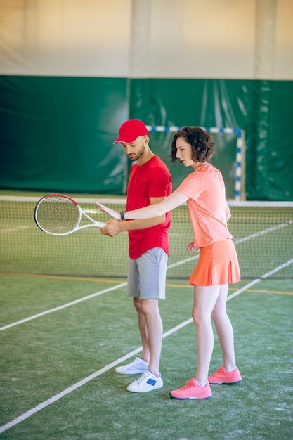 Workout. Man in a red cap and with a racket having a workout with his coach