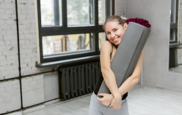 Workout routine concept Happy slim woman smiling holding yoga mat in hand standing in yoga studio prepare training