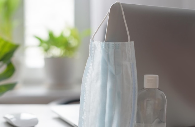 Workplace at home by the window with a laptop protective face mask and sanitizer concept of quarantine during coronavirus pandemic in the world