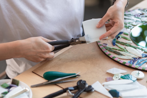 Workplace of the mosaic master womens hands holding tool for mosaic details in the process of making...