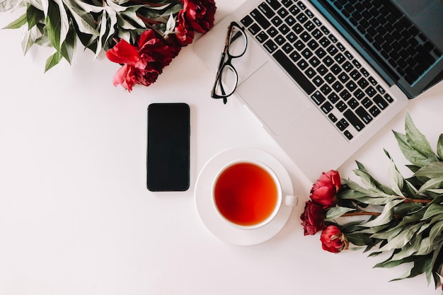 Workplace top view laptop cup of tea phone peonies glasses