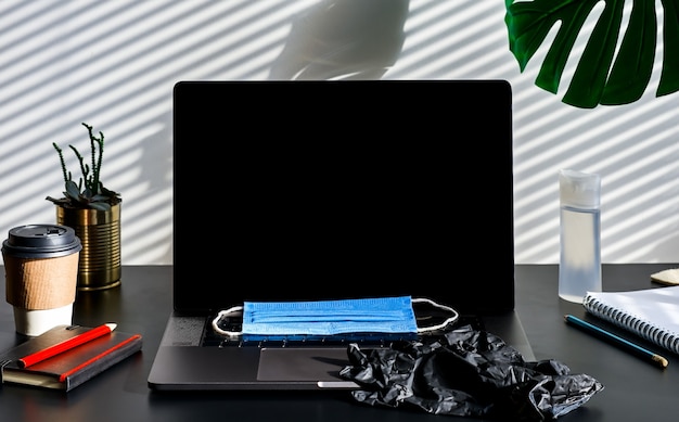 Workplace with computer, medical mask and hand sanitizer on table in home office.