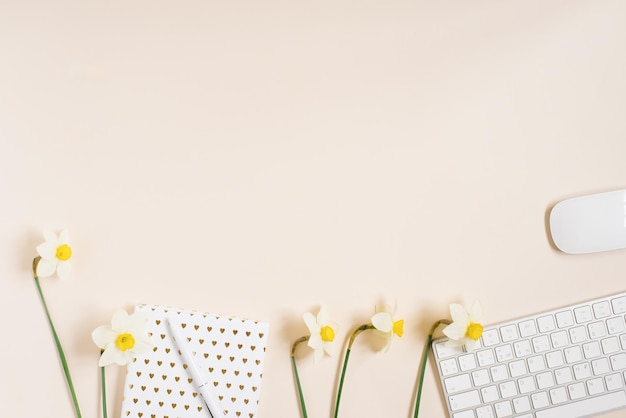 Workplace with a diary pen keyboard mouse and daffodil flowers on a light background