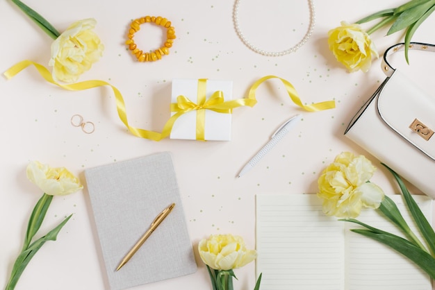 Workplace with a notebook and a pen yellow tulips a bracelet a womans handbag on a light background