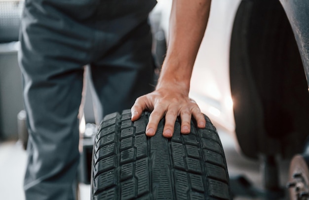 Works with tire Adult man in grey colored uniform is in the automobile salon