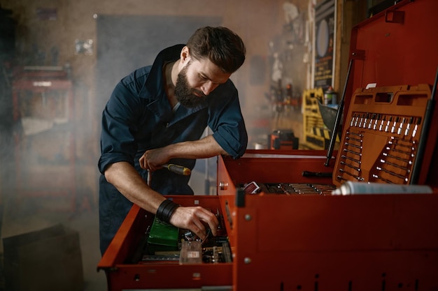 Workshop man worker looking for special tools in box for repair motorcycle. Male mechanic or technician in garage