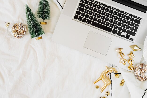 Workspace in bed with laptop and Christmas decorations. Holiday concept. Flat lay, top view