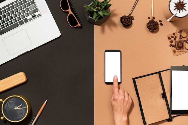 Workspace coffee design. Hand point on mobile phone blank white screen. Flat lay top view desk with stationery, arabica bean, digital device.