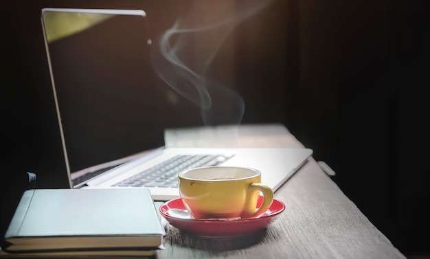 Workspace concept in dark tone color with laptop and cup of coffee on wooden table.