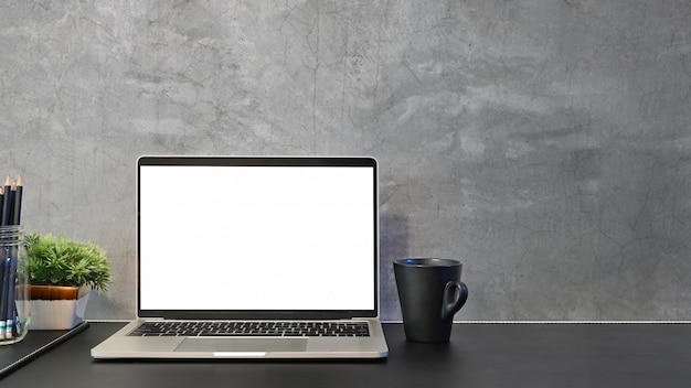 Workspace laptop empty screen, coffee, pencil on black leather table and loft wall.