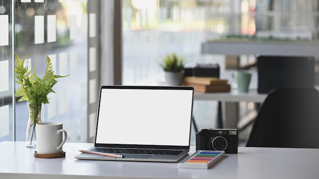 Workspace mockup laptop computer on table with camera, coffee and plant in modern office room.