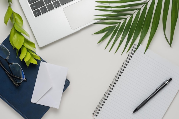 Workspace with blank notebook laptop office supplies green leaf and eyeglasses on white background Flat lay top view office table desk