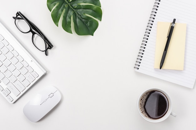 Workspace with computer keyboard, office supplies, green leaf, and coffee cup on white