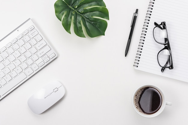 Workspace with computer keyboard, office supplies, green leaf, and coffee cup on white