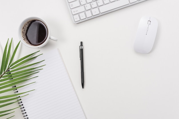 Workspace with computer keyboard, office supplies, green leaf, and coffee cup