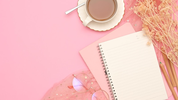 Workspace with empty notepad cover teacup dried flowers and copy space on pink background top view