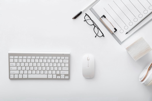 Workspace with keyboard mouse glasses papers. Flat lay White desk office workplace pc computer. White table silver keyboard top view with copy space.