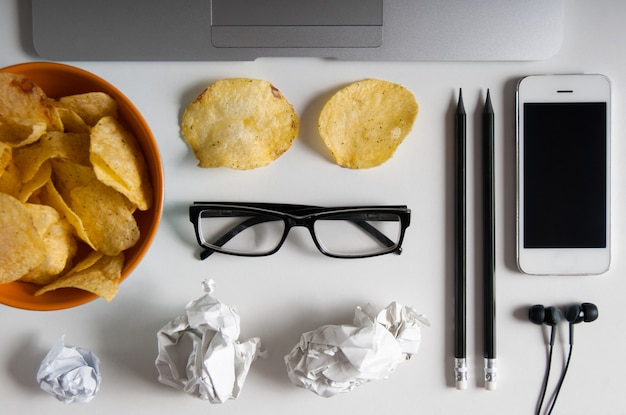 Workspace with laptop,crumpled paper and bowl of chips on wood table. Bad habits concept