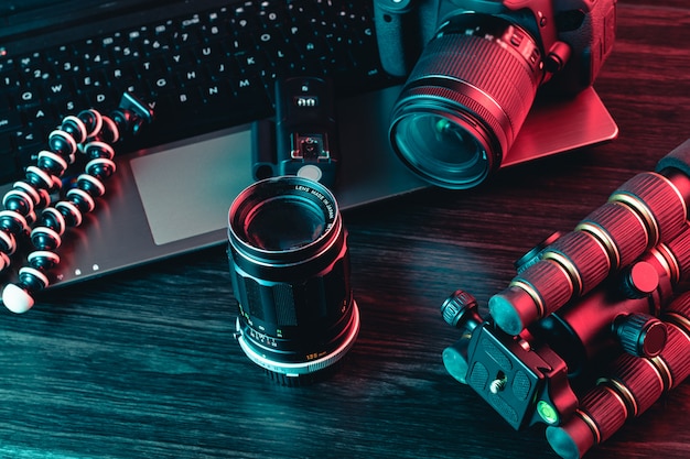 A workspace with laptop, modern camera, lens, tripod and a pen