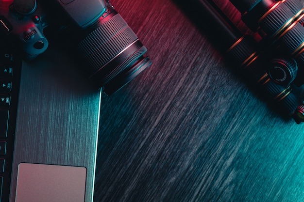 A workspace with laptop, modern camera, lens and tripod on a wood table.