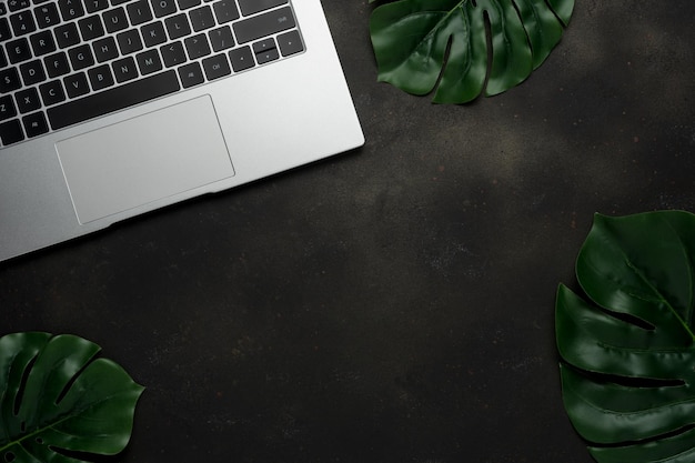 Workspace with laptop and palm leaves on black background Flat lay top view office table desk