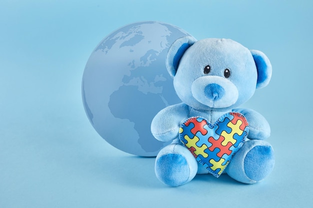 World autism awareness concept with teddy bear holding puzzle or jigsaw pattern heart on blue backgr